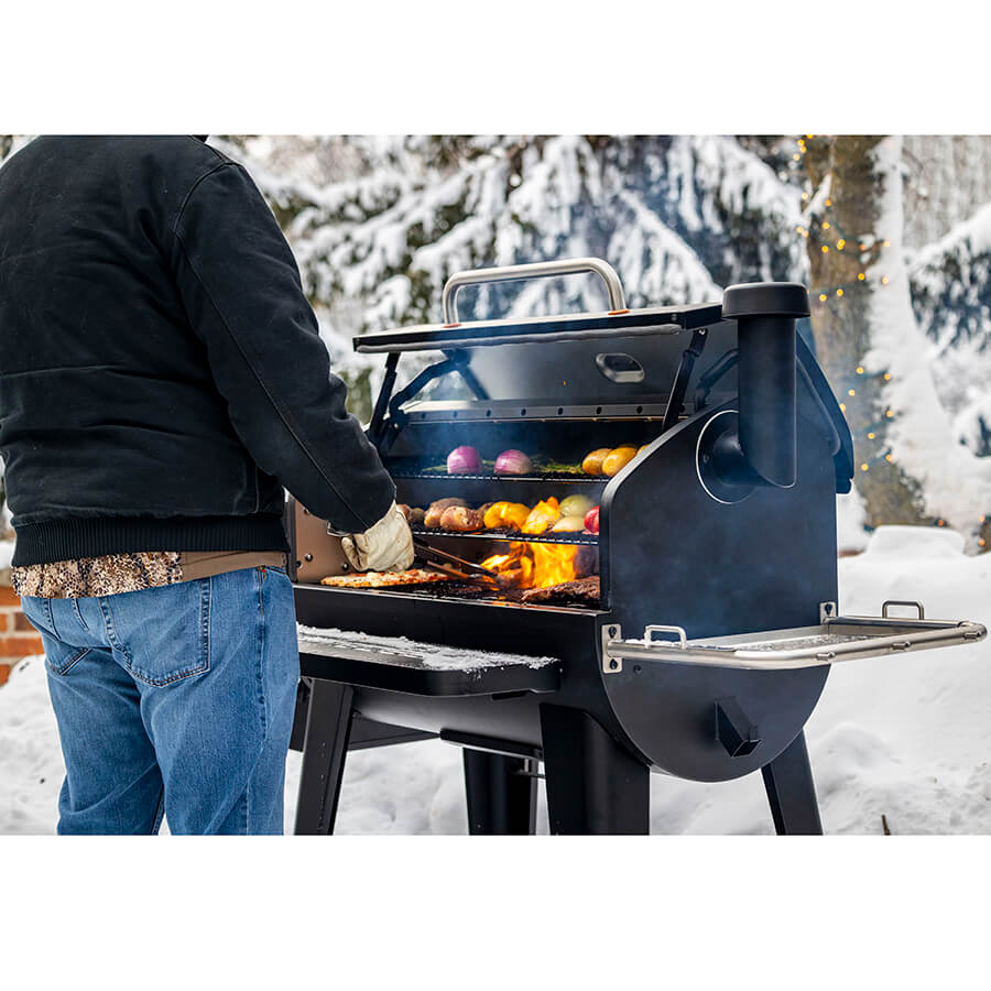 Man grill standing outside in a winter setting grilling meats and veggies on the Pit Boss Sportsman 1600 Wood Pellet Grill.