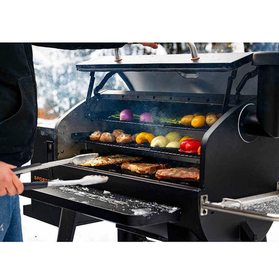 Man opening the hood of a Pit Boss Sportsman 1600 Wood Pellet Grill. Meats and veggies being smoked on all three cooking racks.