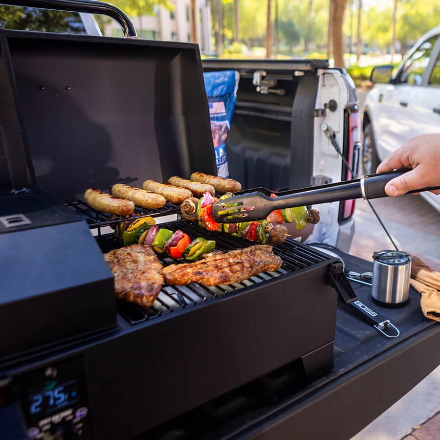 Pit Boss Portable Tabletop Pellet Grill, Black. Flipping veggie skewers that are being grilled on back of truck tailgate