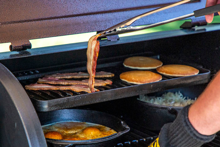 black cast iron griddle on grill grate with pancakes and bacon on it
