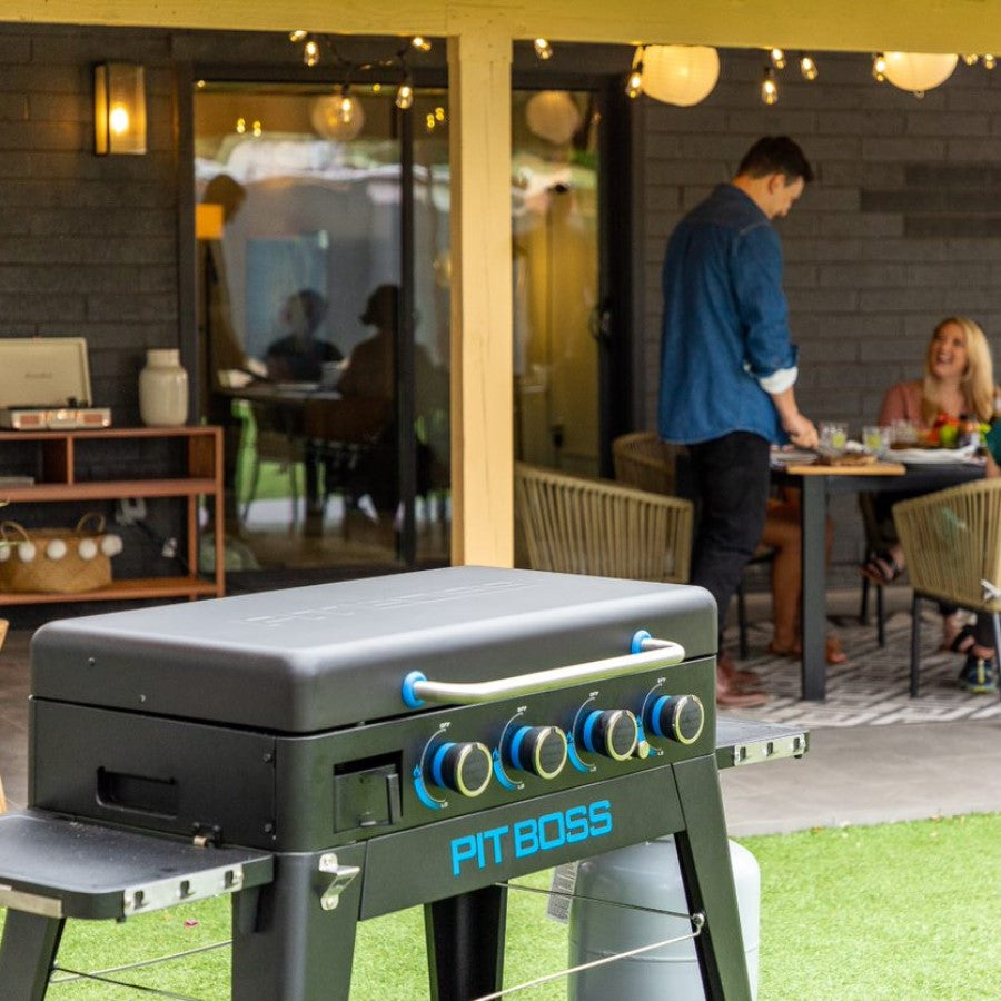lifestyle_8, Black griddle with bright blue and silver accents and a large blue Pit Boss logo on front. Family enjoying a meal with griddle in foreground