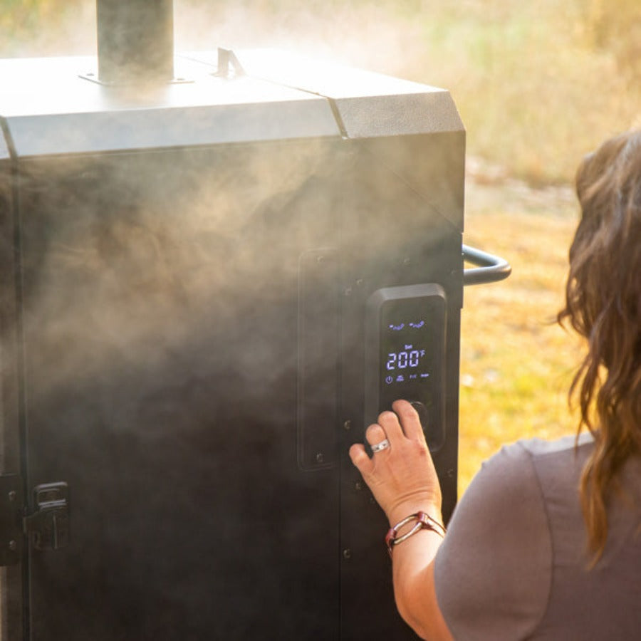 lifestlye_7, Black smoker with small Pit boss logo on transparent door and engraved "Pro Series" on front. Up close of woman setting temperature on smoker's digital control board