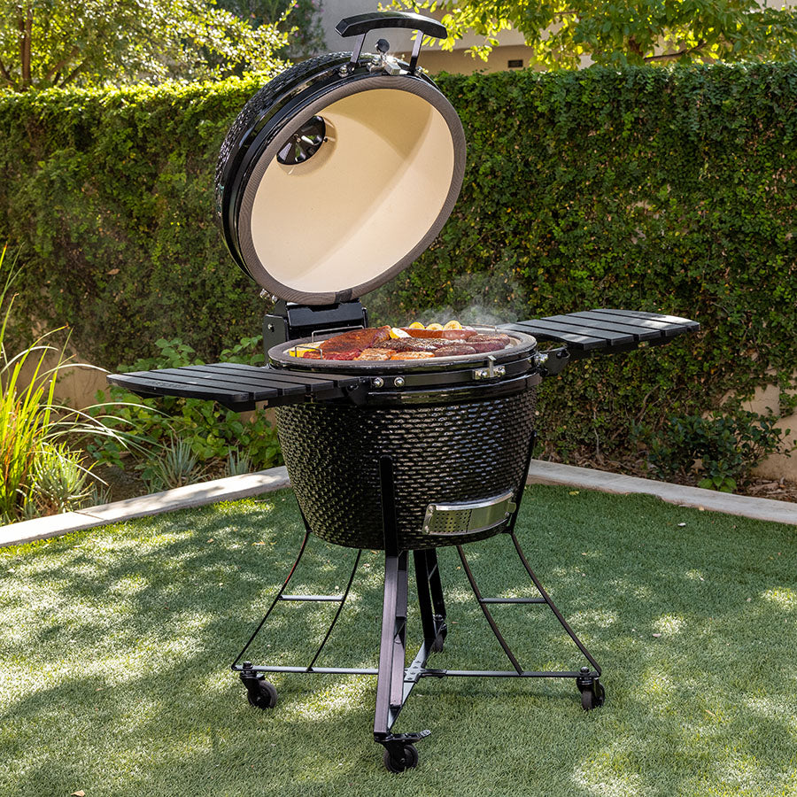 lifestyle_2, All black charcoal grill with bumpy texture and silver accents. Shown in backyard grilling meat and veggies