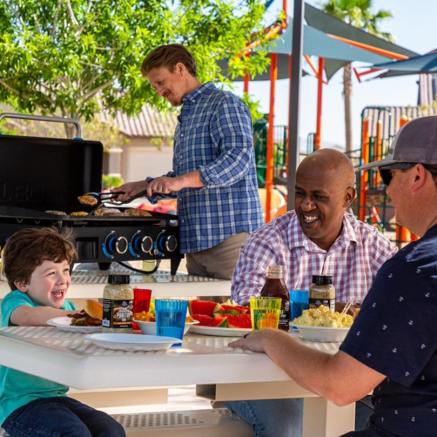 Family enjoying food made on the griddle around a picnic table.