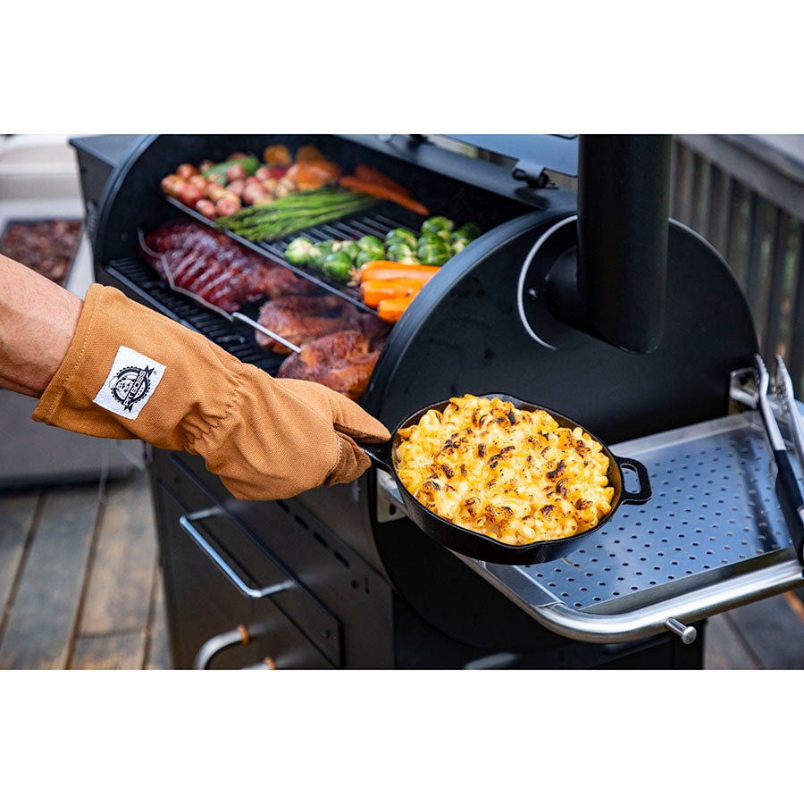 using gloves to handle a cast iron pan of mac and cheese fresh off of the grill