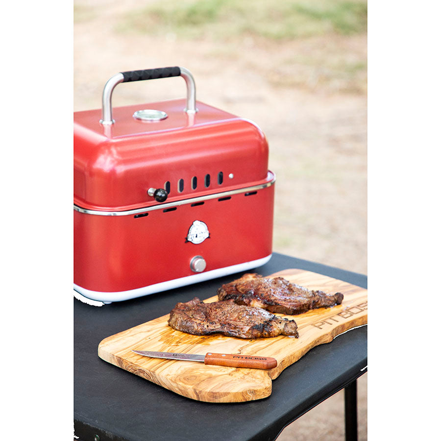 lifestyle_1, Red grill with black and silver accents and a small Pit Boss logo. Pictured on outdoor table with grilled meat
